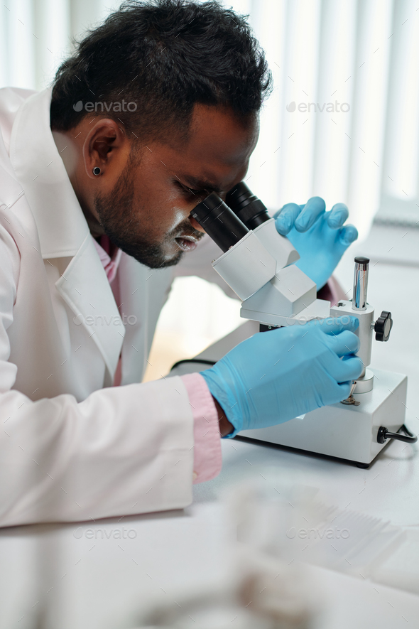 Side view of young African American male scientist looking in microscope - Stock Photo - Images