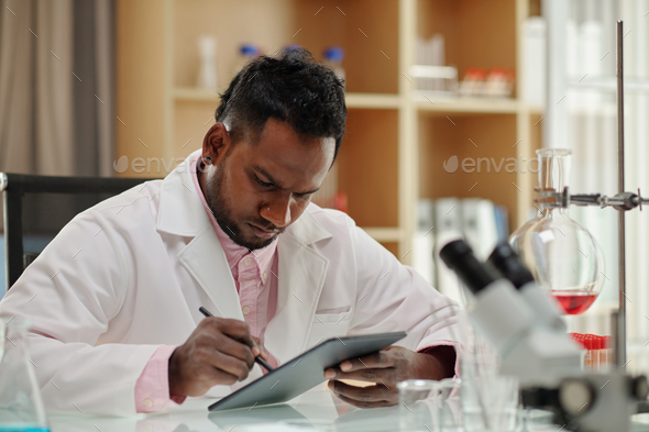 Serious African American clinician or researcher using tablet by workplace - Stock Photo - Images