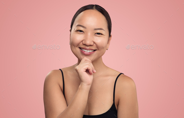 Cheerful Asian woman touching chin in studio - Stock Photo - Images