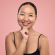 Cheerful Asian woman touching chin in studio - PhotoDune Item for Sale