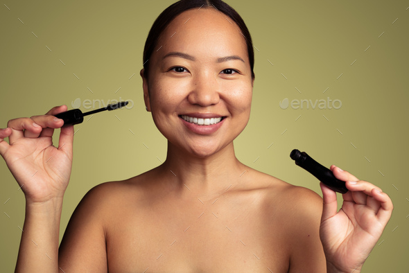 Smiling Asian woman with mascara in studio - Stock Photo - Images