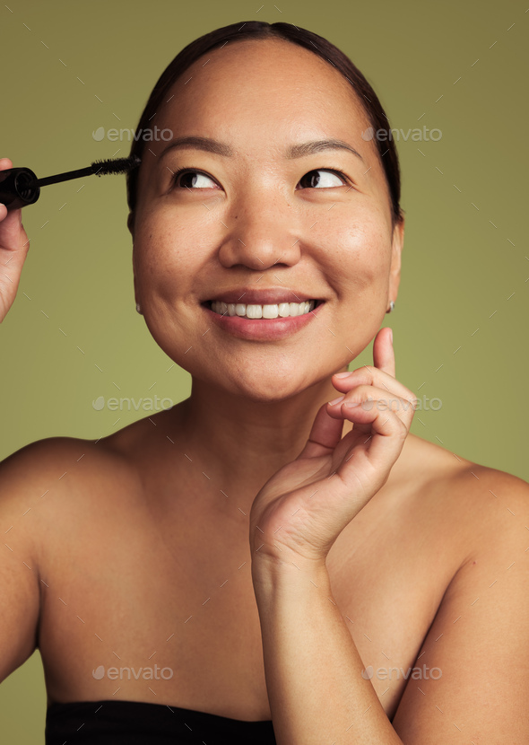 Smiling ethnic woman applying mascara on eyelashes in studio - Stock Photo - Images