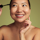 Smiling ethnic woman applying mascara on eyelashes in studio - PhotoDune Item for Sale