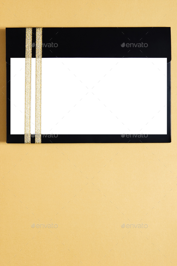Black envelope mockup, Flat Lay, on gold background with copy space. Tied with gold ribbon