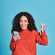 Young happy latin woman winner holding mobile cell phone isolated on blue. - PhotoDune Item for Sale