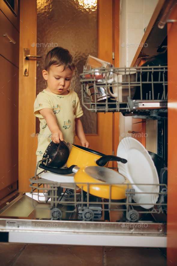 Child puts dirty crockery in the home dishwasher. Mom's little helper ...