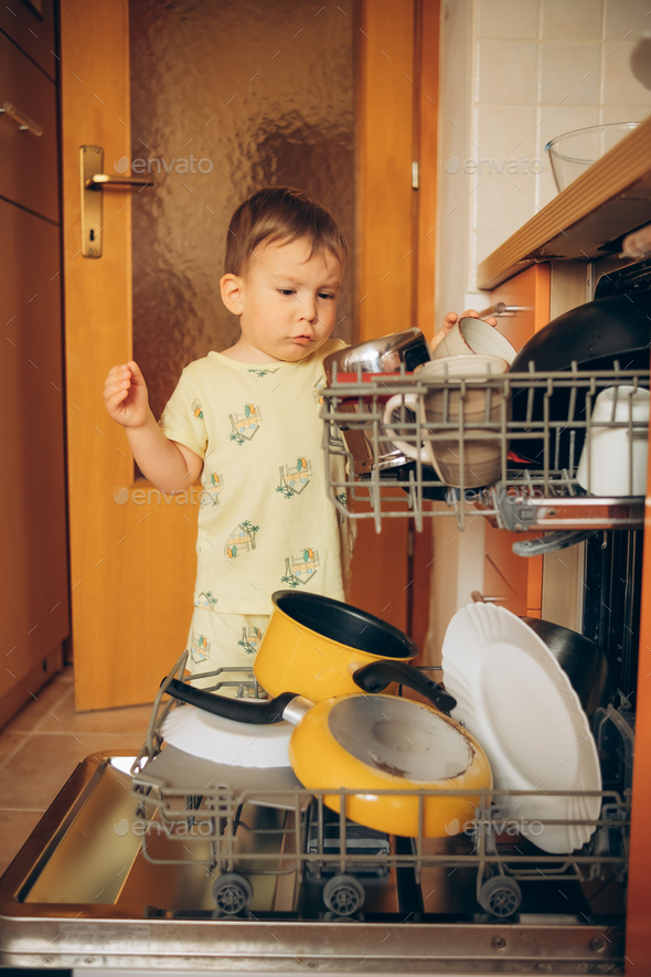 Child Puts Dirty Crockery In The Home Dishwasher. Mom's Little Helper 