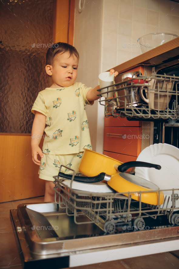 Child puts dirty crockery in the home dishwasher. Mom's little helper ...