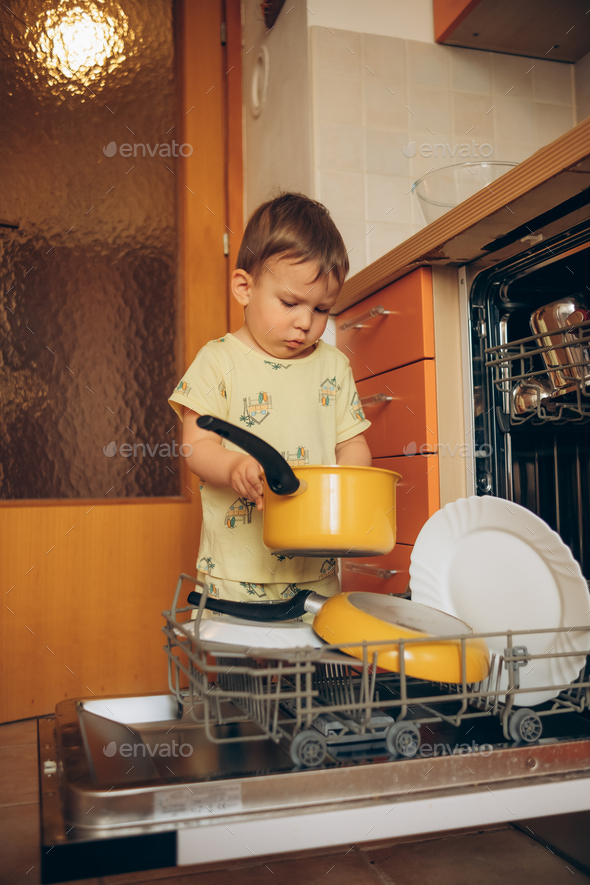 Child puts dirty crockery in the home dishwasher. Mom's little helper ...