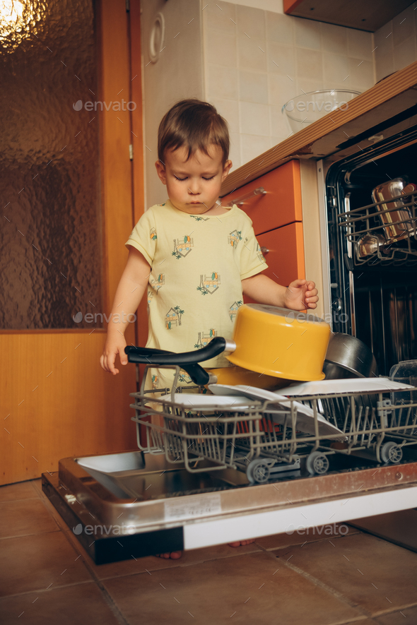 Child puts dirty crockery in the home dishwasher. Mom's little helper ...