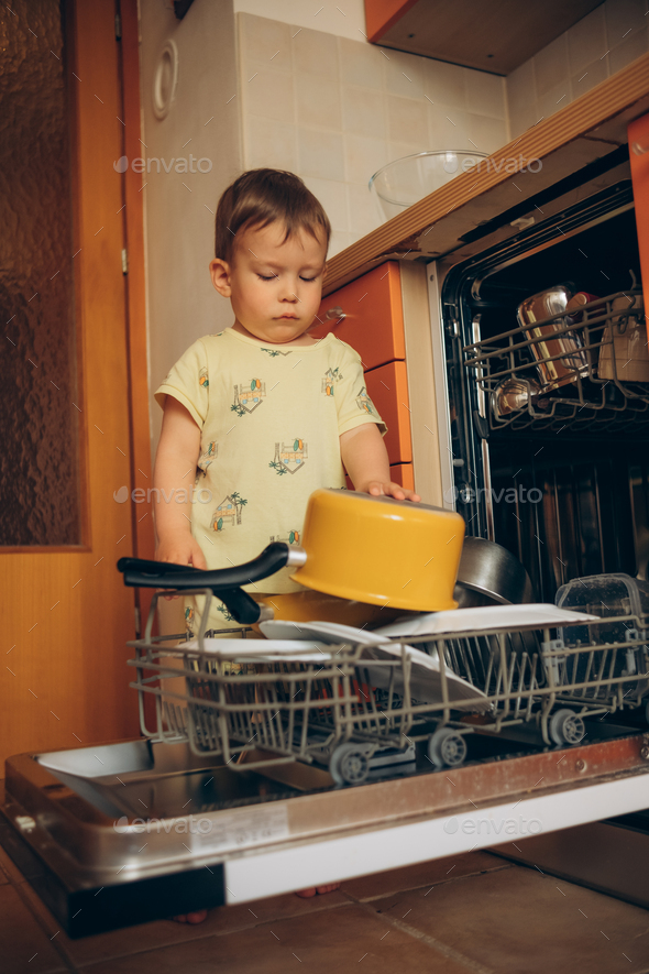 Child puts dirty crockery in the home dishwasher. Mom's little helper ...