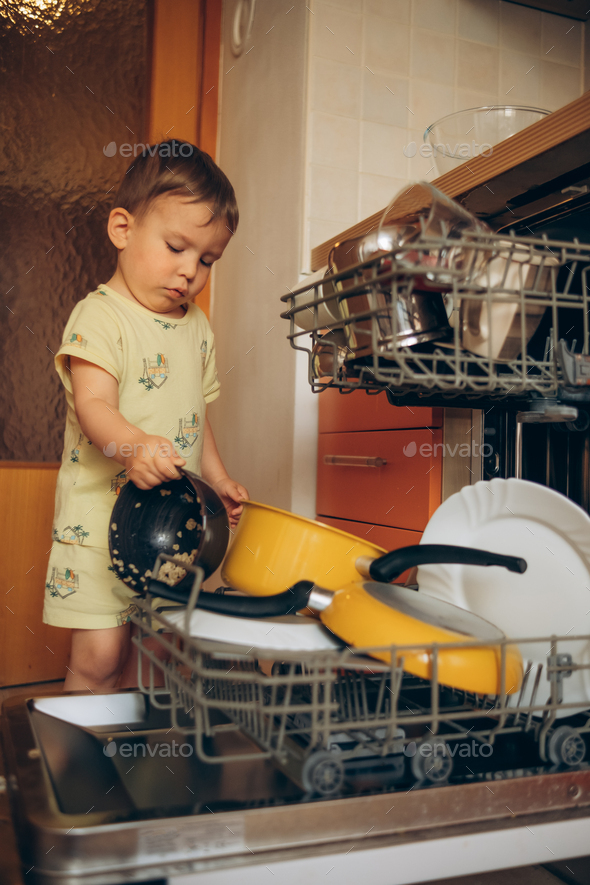 Child puts dirty crockery in the home dishwasher. Mom's little helper ...