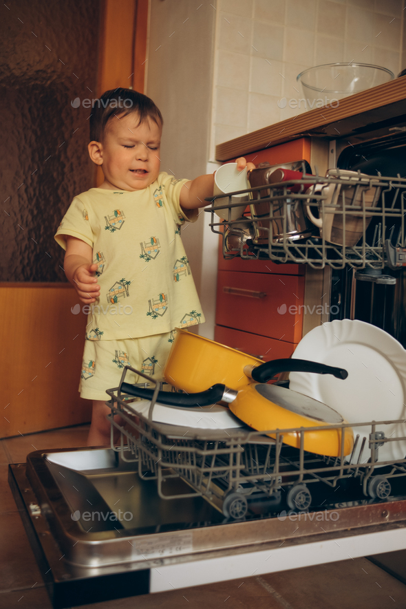 Child puts dirty crockery in the home dishwasher. Mom's little helper ...