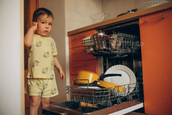 Child puts dirty crockery in the home dishwasher. Mom's little helper ...