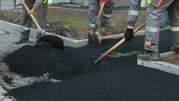 Workers pour asphalt with a shovel . Loosening and leveling of heated asphalt on the sidewalk