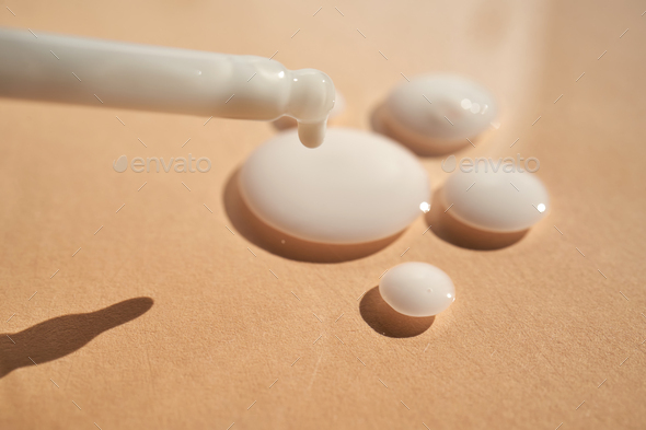 Drops of white cosmetics on a beige background with a dropper. - Stock Photo - Images
