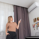 Young woman switching on air conditioner while sitting in armchair at home - PhotoDune Item for Sale