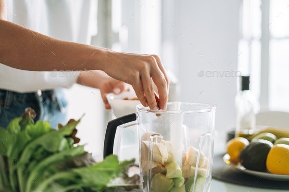 Young slim woman in white t-shirt and blue jeans cooking smoothie healthy food in kitchen at home - Stock Photo - Images
