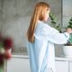 Young woman in blue shirt with spray with water in hands takes care of houseplant in kitchen at home - PhotoDune Item for Sale