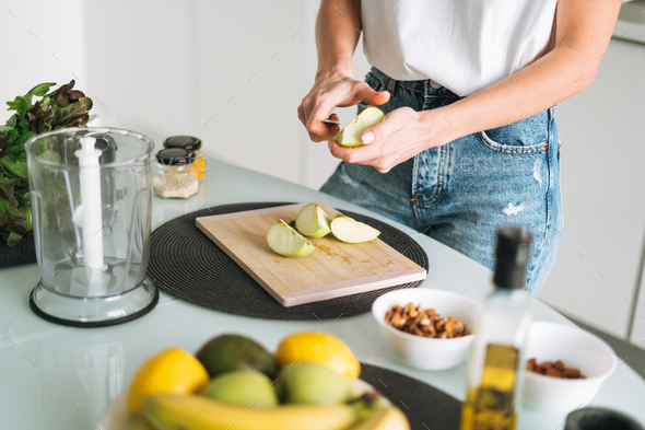 Young slim woman in white t-shirt cooking smoothie with apples healthy food  in kitchen at home Stock Photo by GalinkaZhi