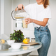 Young woman in white t-shirt and blue jeans pouring fruit smoothie healthy food in kitchen at home - PhotoDune Item for Sale