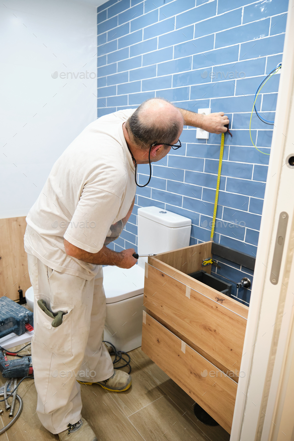 Senior mason measuring with a measure tape to install bathroom furniture.