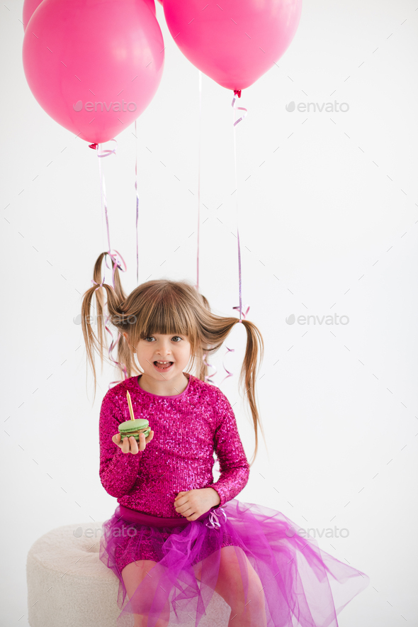 Funny kid girl celebrating birthday with balloons and cake in room over white - Stock Photo - Images