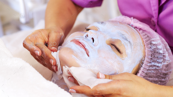 Cosmetologist removing  a mask scrub from female face. Woman in a spa salon on cosmetic procedures.  - Stock Photo - Images