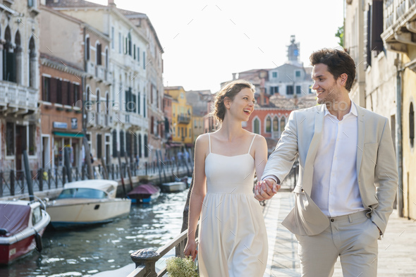 Italy, Venice, happy bridal couple walking hand in hand at morning twilight