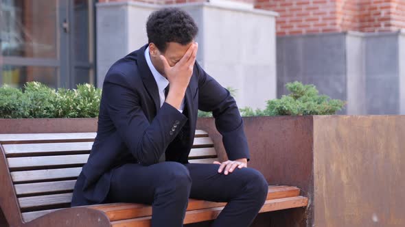 Tense African Businessman with Headache Sitting on Bench alt