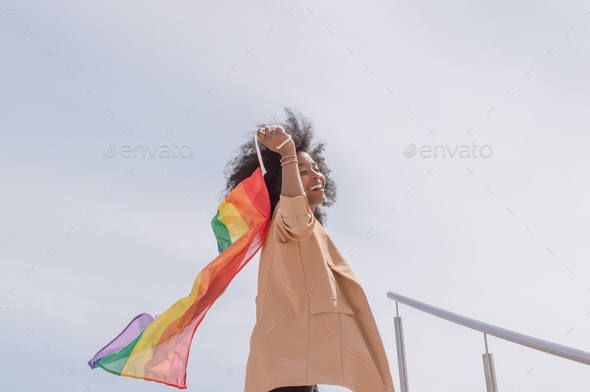 young brunette latina woman with afro smiles and dances contentedly smiling a gay pride flag