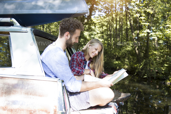 Smiling young couple with map and canoe in car at a brook