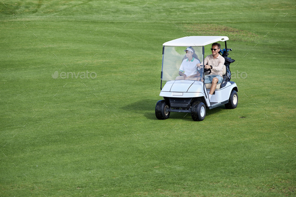 Wide angle view of couple driving golf cart on green field minimal