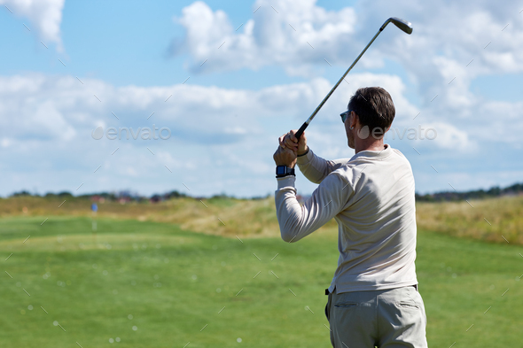 Back view of man playing golf and swinging golf club in sunlight at sports club - Stock Photo - Images
