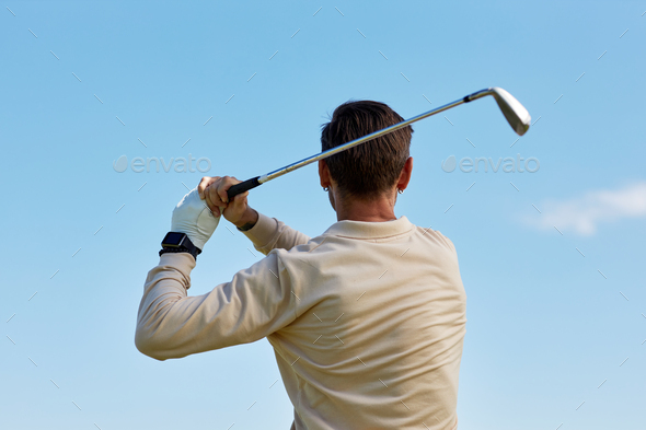 Back view of man swinging golf club against blue sky - Stock Photo - Images