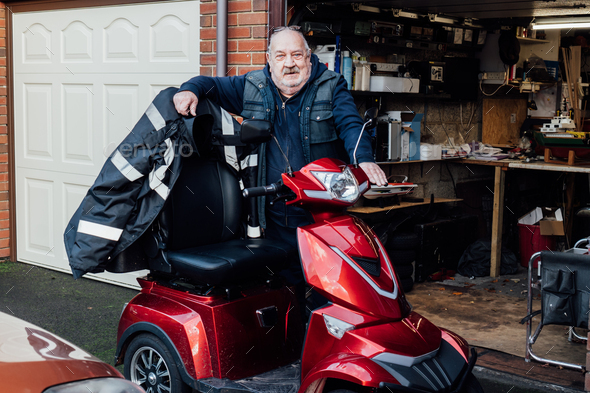 Portrait of elderly man standing near mobility scooter on the background of his garage.