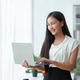 Beautiful Asian business woman standing holding a laptop in the office - PhotoDune Item for Sale