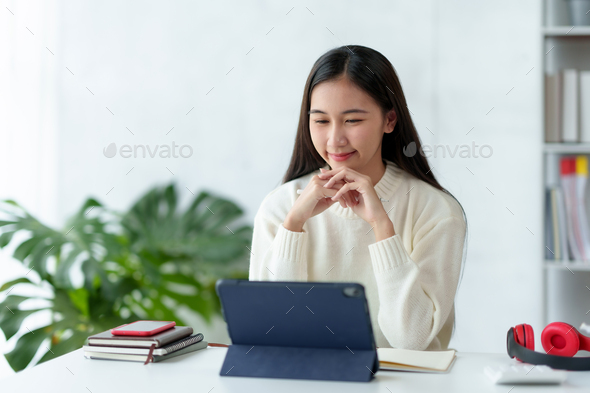 Attractive Asian business woman sitting at work happily working using tablet at office and smiling
