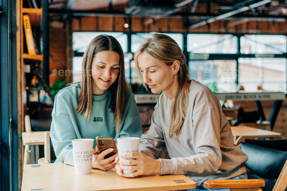 Two cheerful smiling women are watching social networks in a mobile phone. - Stock Photo - Images