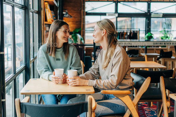 Two female friends are chatting and drinking coffee while sitting in a coffee shop. - Stock Photo - Images