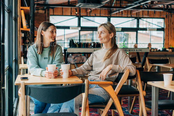 Two cheerful smiling women friends are discussing while sitting in a cafe. - Stock Photo - Images