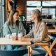 Two female friends are chatting and drinking coffee while sitting in a coffee shop. - PhotoDune Item for Sale