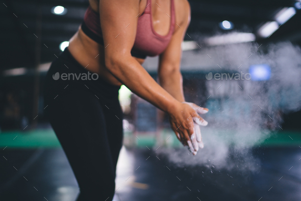 Unrecognizable muscular woman clapping hands with talc and preparing for weightlifting at gym,