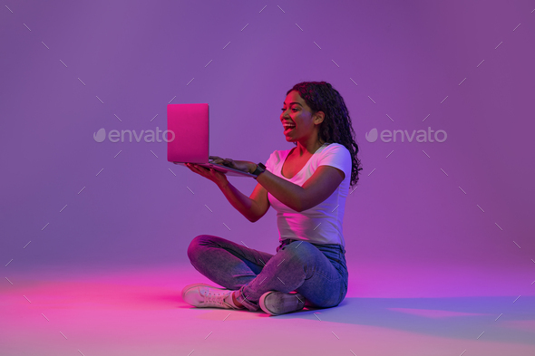 Happy Excited Black Lady Looking At Laptop Screen In Neon Light