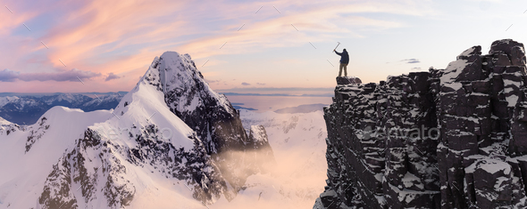 Adventurous Man Hiker standing on top of icy peak with rocky mountains in background. - Stock Photo - Images