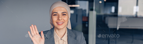Smiling muslim businesswoman in hijab waving hi during work in modern office - Stock Photo - Images