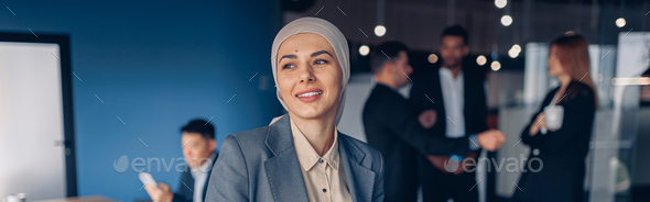 Smiling muslim businesswoman in hijab working on digital tablet while standing in modern office - Stock Photo - Images
