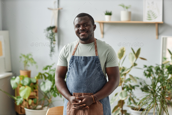 Smiling black man as gardener wearing apron posing indoors looking at camera - Stock Photo - Images