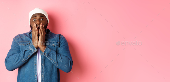 Alarmed and worried Black man staring at bad accident, gasping and standing in panic over pink
