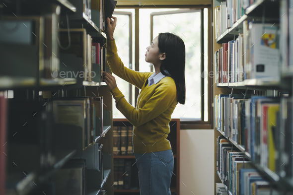 Student choosing and reading book at library. - Stock Photo - Images